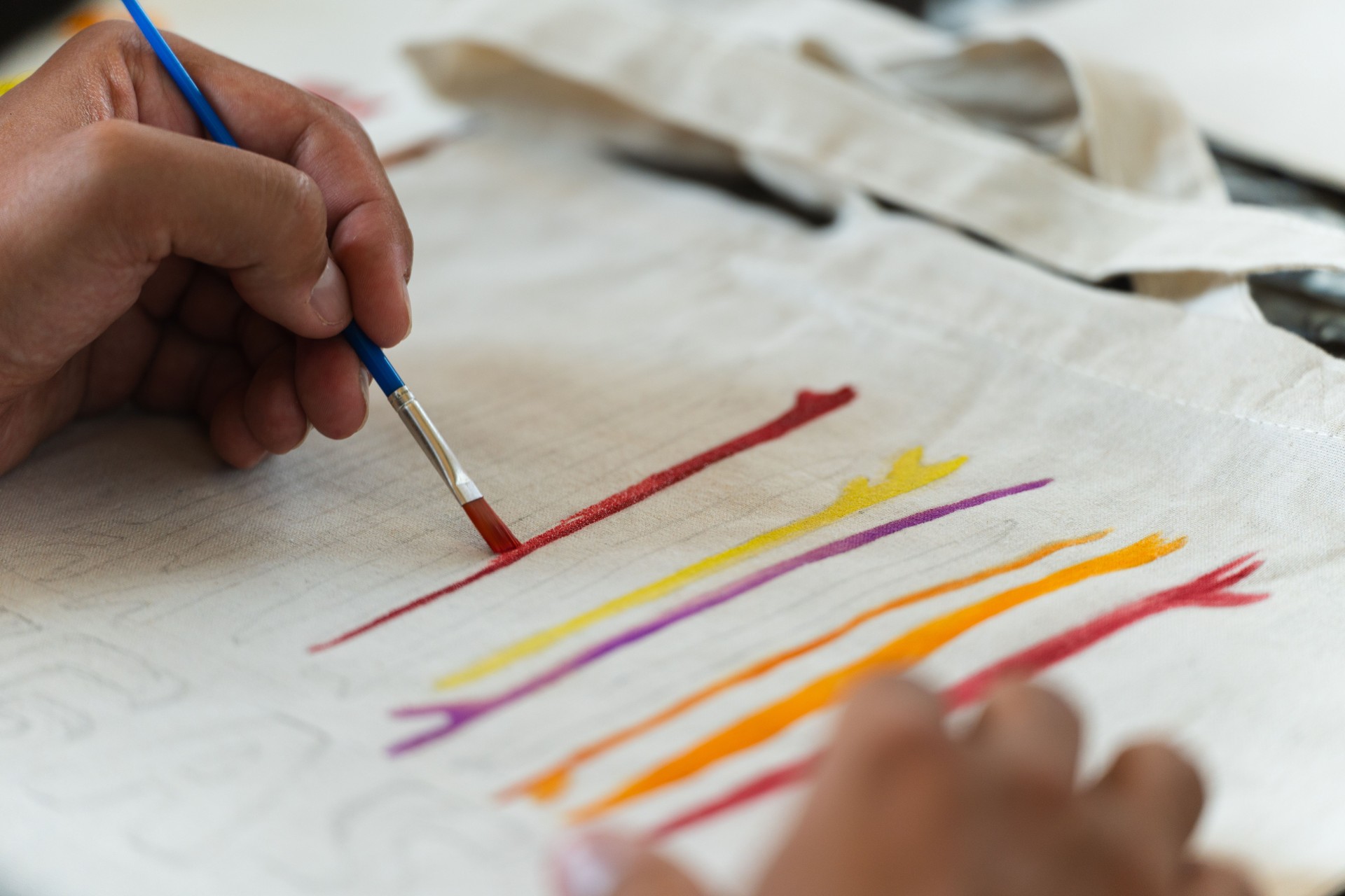 Detail shot of a hand painting a recycled bag with a brush and multiple colors