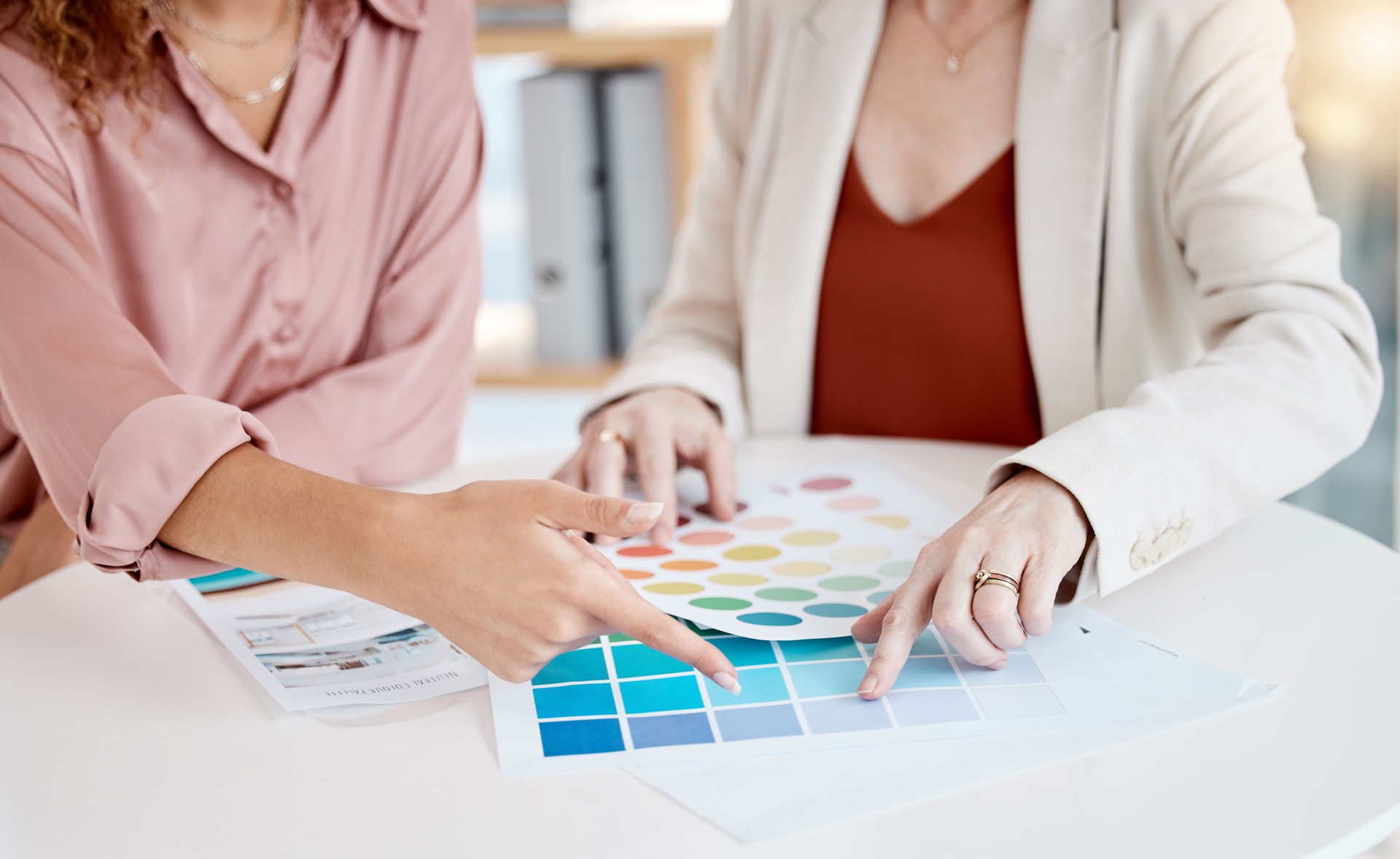 Closeup of two businesspeople looking at colour swatches while in a meeting together at work. Businesswomen pointing their fingers and choosing between different colours for a design in an office at work